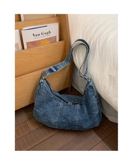 Detailed close-up of blue denim crescent bag with white stitching and metal buckle