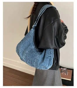 Detail of a large blue washed denim hobo bag featuring a crescent shape and wide shoulder strap