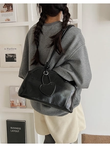 Close-up of black glossy PU leather shoulder bag with matching heart charm and knotted strap
