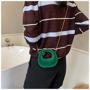 Green velvet round mini crossbody bag with gold chain strap shown on model's shoulder