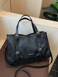 Black pleated leather tote bag with vertical textures and fashion buckles on wooden desk