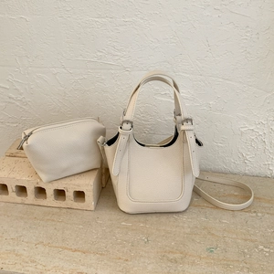 Detail of cream lychee leather bucket bag and zipper pouch set on stone surface