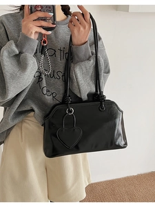 Detail of black glossy tote bag with heart charm and thin straps on a model