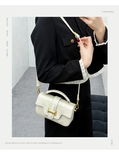 Close-up of cream white handbag with gold H-shaped buckle worn by model in a studio