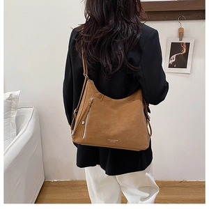 Rear view of a model wearing a brown leather shoulder bag with silver zipper detail