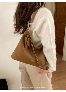 Detail of a brown leather tote bag featuring a gold chain strap and a small side pouch
