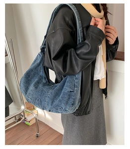 Detail of vintage washed blue denim crescent bag with wide strap and zip closure