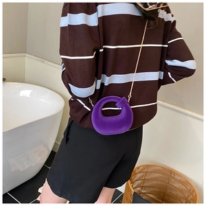 Detail of a purple velvet semi-circular crossbody bag with a gold chain strap on a model
