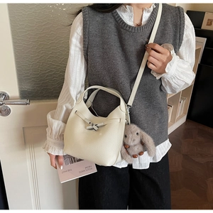 Detail of creamy white bucket bag in lychee leather texture with a cute plush rabbit charm