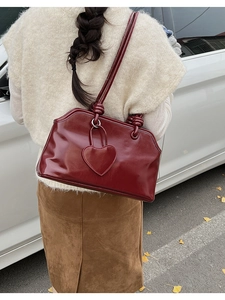 Detail of burgundy glossy leather handbag with heart charm and knotted handle design