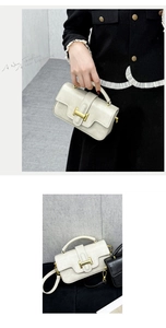 Close-up of stylish handbag with gold H-shaped lock, top handle and detachable strap