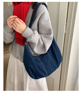 Close-up of a large denim crescent shoulder bag with white stitching detail and retro style