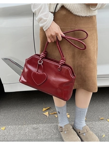 Close-up of wine red faux leather handbag featuring heart pendant and knot handle detail
