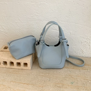 Light blue lychee texture bucket bag and matching rectangular pouch set on stone tiles