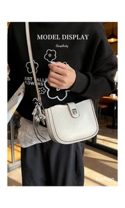 Chic cream-colored bucket bag with metallic charms and magnetic closure on a model
