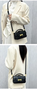 Detailed view of a black leather square handbag featuring a prominent gold H-shaped buckle