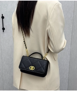 Close-up of black quilted leather crossbody bag with golden chain strap on model