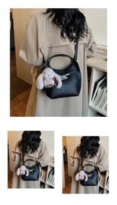 Close-up of black lychee leather bucket bag with silver clasp and plush rabbit charm