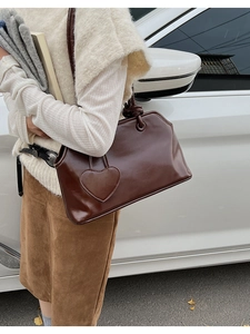 Detail of dark brown leather tote bag featuring heart pendant and knot strap design