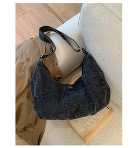 Detail of dark grey retro denim hobo bag featuring wide strap on white sofa