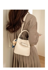 Detail view of cream bucket bag with lychee texture and cute bear charm decoration