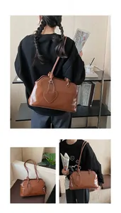 Detail of glossy brown tote bag featuring knotted handles and a heart leather charm