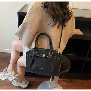 Close-up of black matte handbag with decorative buckle and adjustable long shoulder strap