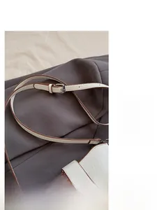Detail of adjustable brown leather shoulder strap with silver metal buckle on a white bag