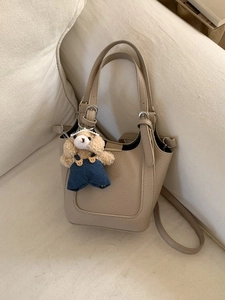 Minimalist beige bucket bag with teddy bear charm on a cozy cream sofa background