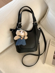 Black lychee pattern bucket bag with detachable strap and cute teddy bear charm on sofa