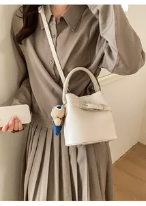 Detail of cream bucket bag with lychee grain leather, metal buckle and bear charm