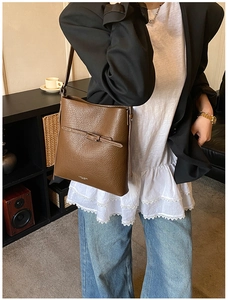 Détail d'un sac seau en cuir grainé marron foncé avec fine boucle porté par un mannequin