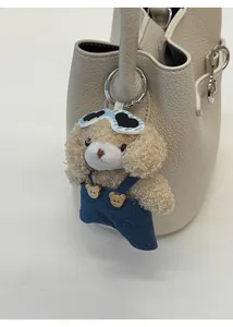 Detail of curly plush puppy charm with heart sunglasses on a beige bucket handbag