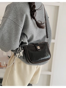 Model wearing a black glossy leather crossbody bag with a silver star charm accessory
