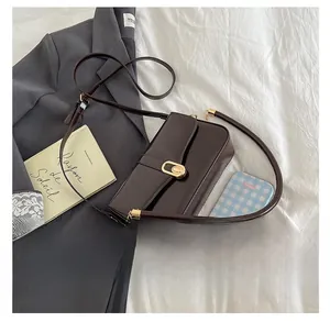 Close-up of a dark brown leather handbag with a gold oval clasp on a white textured surface