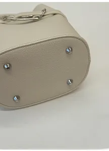 Detail view of reinforced wide bag base with silver anti-wear metal studs on beige leather