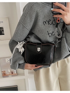 Detail of black glossy saddle bag featuring silver clasp and woven shoulder strap