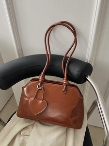Vintage brown shoulder bag in glossy PU leather with heart charm on a black chair