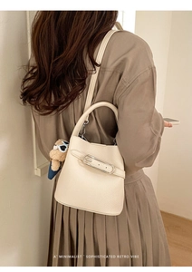 Minimalist beige pebble leather bucket bag with cute bear charm worn as a crossbody