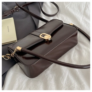 Detail of a dark brown glossy leather crossbody bag with a gold oval metal buckle