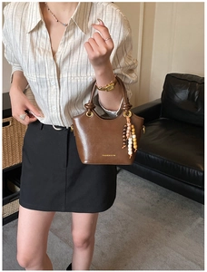 Detail of a brown leather handbag with gold lettering and decorative beaded keychain charm