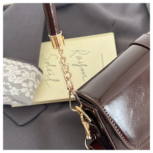 Detail of dark brown glossy leather bag with gold chain strap and French retro aesthetic