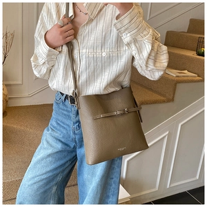 Sac seau en cuir taupe à motif litchi porté par un mannequin dans un style décontracté