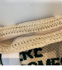 Close-up of beige woven straw tote bag featuring smooth metal zipper and green lettering