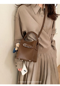 Brown lychee leather bucket bag detail with silver hardware and blue bear charm pendant