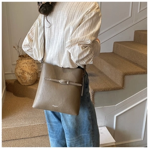 Détail du sac seau en cuir grainé montrant la texture fine et le logo doré au bas