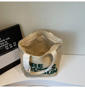 Detailed view of straw tote bag with green Here Comes The Sun embroidery and zipper