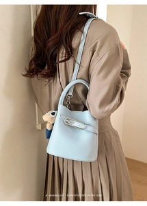 Light blue bucket bag with leather strap and bear charm worn by model in retro outfit