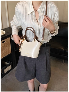 Detail of cream bucket bag featuring brown knotted handle and wooden bead charm
