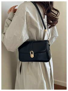 Detail of black glossy leather crossbody bag with golden oval clasp and chain strap